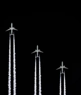 Three aircraft in formation with contrails against a dark sky